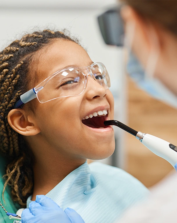 Little girl in protective glasses opening her mouth while dentist curing her teeth.